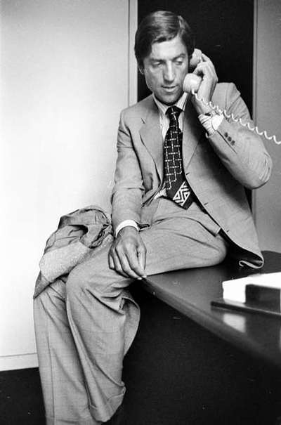 Nino Cerruti in his office sitting on desk making phone call
