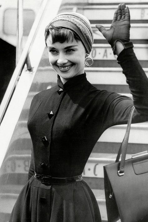 Elegant style icon wardrobe essentials: Audrey Hepburn in little black dress, Heathrow Airport in London, 21 May 1953.