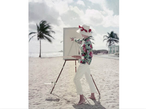Model standing on a beach in front of an easel, in a patterned shirtand pants by Queen Casuals and a Sally Victor. straw hat.Glamour, April 1, 1960  © Frances McLaughlin-Gill